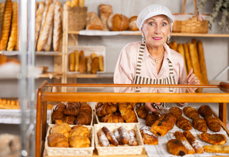 Selling fresh croissants in bakery - smiling female baker places hot croissants on displayの写真素材