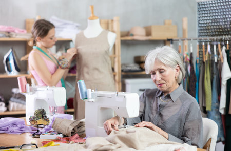 Mature woman working at sewing machine with assistant in the backgroundの写真素材