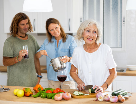 Cheerful couple and old woman drinking wine and cooking in the kitchen at homeの写真素材