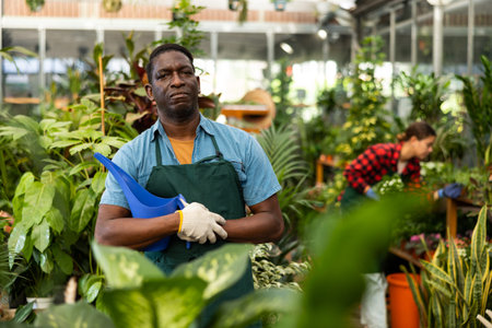 African american salesman with watering can among ornamental plants in garden store