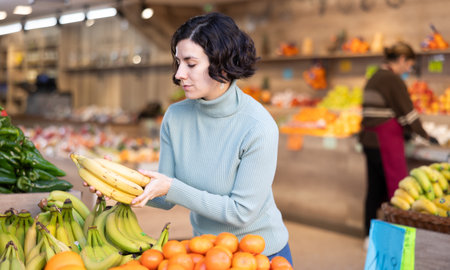 Female shopper carefully selects fresh bananas and other fruits in grocery supermarketの写真素材