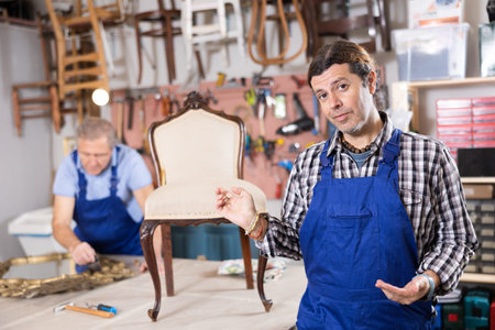 Skilled middle-aged male furniture repair specialist in uniform restoring Victorian chair during workday in workshopの写真素材