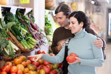 Couple man and woman choosing tomatoes in vegetable shopの写真素材