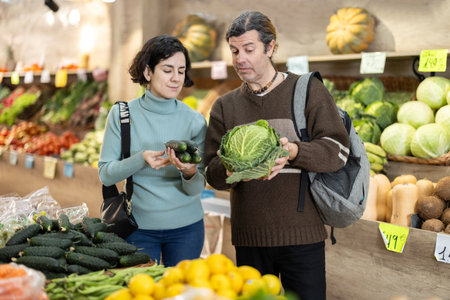 Married couple selects fresh vegetables at supermarket counterの写真素材