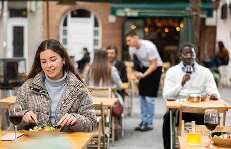 Young woman sitting on the terrace of a restaurant and eating saladの写真素材