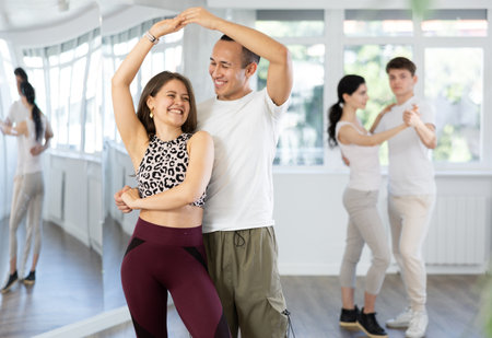 Positive young woman and man practicing waltz dance moves in pair during group training in dancing studioの写真素材