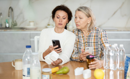 Adult daughter and elderly mother scan barcode on food package together using smartphoneの写真素材