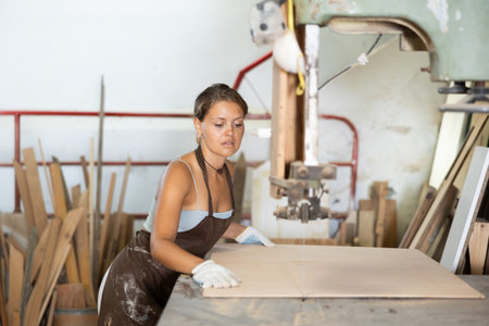Girl employee of workshop cuts wooden board into parts using sawの写真素材