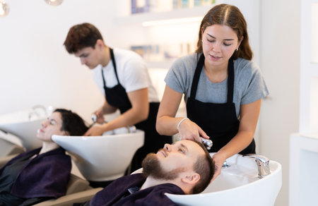 Young female hairdresser washing hair of male clientの写真素材