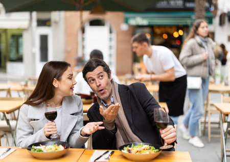 Couple having a conversation and enjoying food and wine at an outdoor restaurant.の写真素材