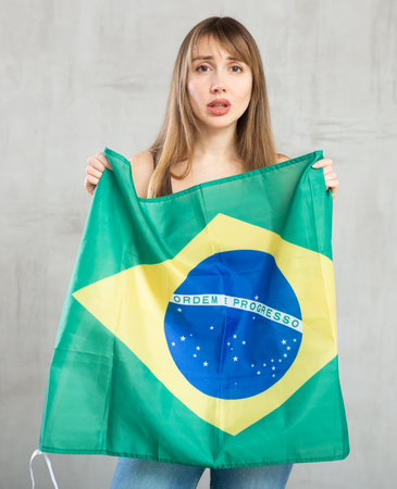Sad young woman holding flag of Brazil against unicoloured backgroundの写真素材