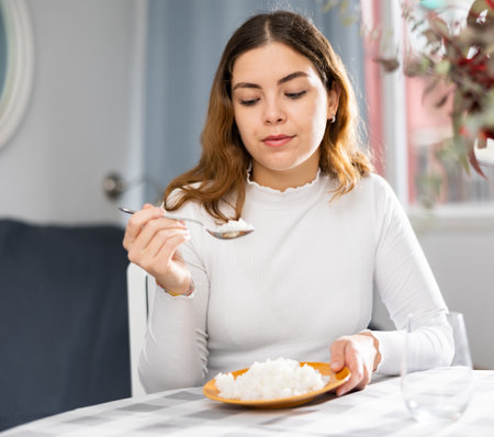 Emotional young woman eating rice at homeの写真素材