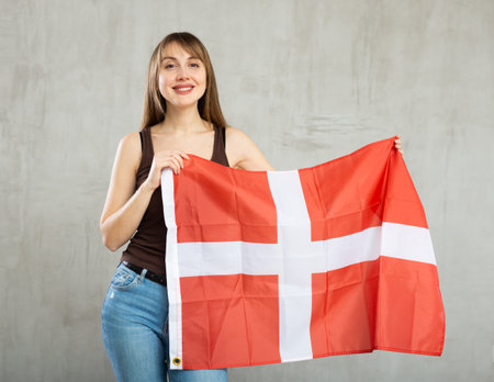 Happy young woman holding flag of Denmark against unicoloured backgroundの写真素材