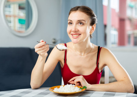 Positive woman eating portion of boiled rice at homeの写真素材