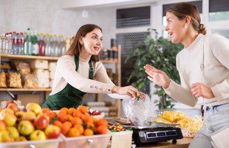 Woman sells and puts candies in bag for young woman, puts them on scale and weighs fruitsの写真素材