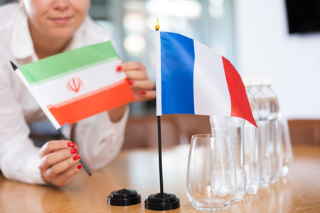 Woman secretary prepares the negotiating table - arranges flags of France and Iranの写真素材
