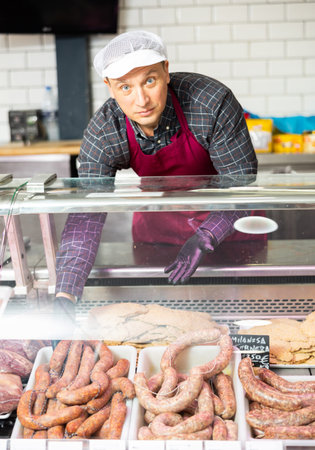 Adult man puts meat sausages in showcase