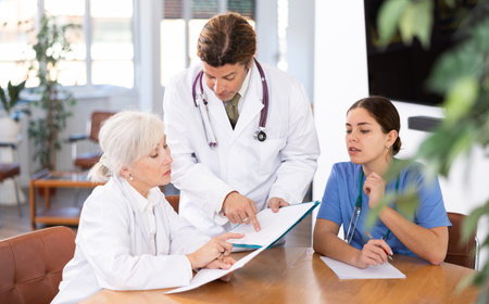 three positive doctors are sitting at table animatedly and actively discussing current workの写真素材
