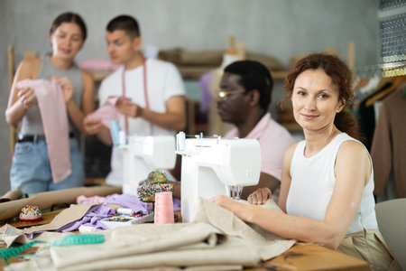 Middle-aged woman sewing while others working with sewing-machine and making details