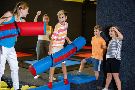 Preteen boy fighting by inflatable pugil sticks with girl