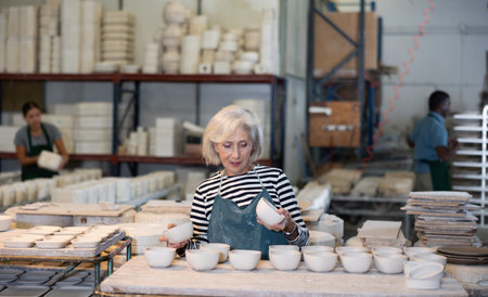Elderly woman ceramist working in pottery workshop