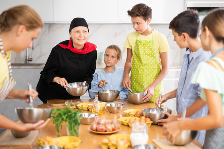 Friendly female chef in black uniform giving culinary lesson to tweensの写真素材