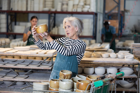 Mature woman ceramist arranging new bowls in workshopの写真素材