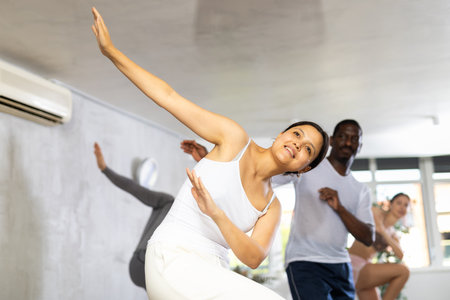 Group of happy sports woman and men in activewear exercising dynamic dancing movemens in gym studioの写真素材