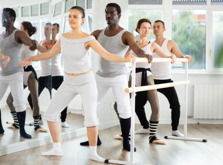 Graceful women and sports men practice at ballet standing at barre in choreography class