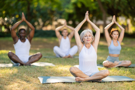 Multinational yoga enthusiasts with senior female coach perform padmasana in parkの写真素材