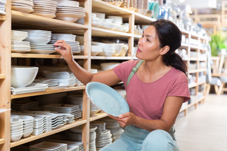 Asian woman choosing plates in storeの写真素材