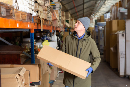 Warehouse worker carrying boxes on racks in in warehouse