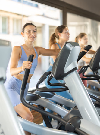 Positive young girl training on elliptical machine in gymの写真素材