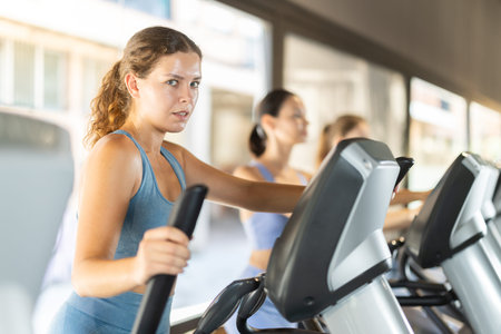 Sportive young girl training on elliptical machine in gym