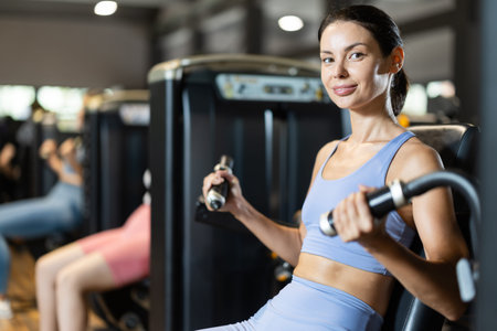 Positive young girl training on arm curl machine in gym