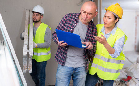 Man with laptop taking to female forewoman in apartment during renovationの写真素材