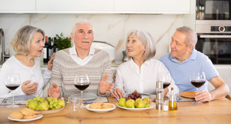 Group of happy elderly people drink red wine and chat at festive table
