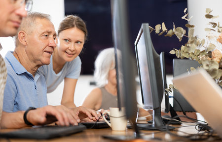 Female teacher explaining computer skills to senior man in nursing home computer classの写真素材