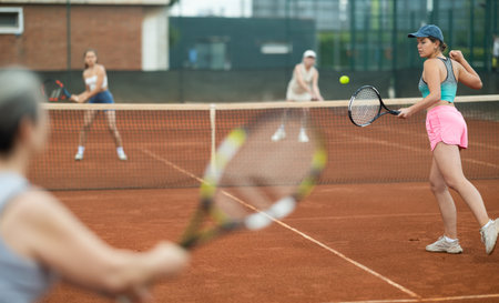 Young and elderly women playing doubles tennisの写真素材