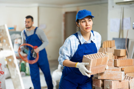 Female builder stacking red bricks at construction site indoorsの写真素材