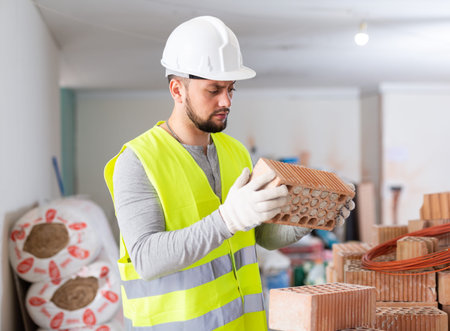 Builder in blue workwear planning erection of partition wall in building under reconstruction,...
