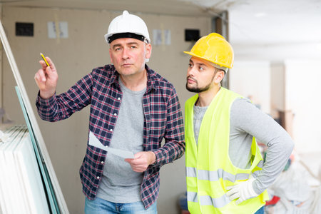 Adult designer with papers talking to contractor in building during renovationの写真素材