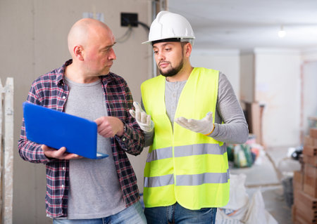 Puzzled builder talking with displeased man with laptop in home during renovationの写真素材