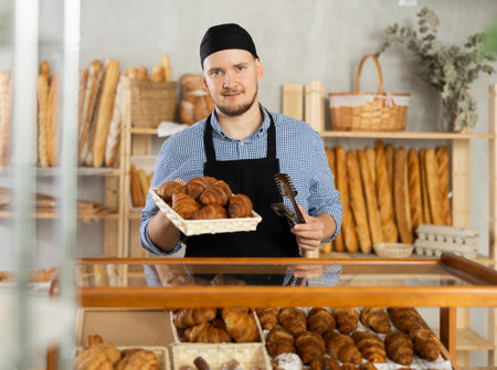 Man seller stands at bakery counter with basket filled with fresh croissants.の写真素材