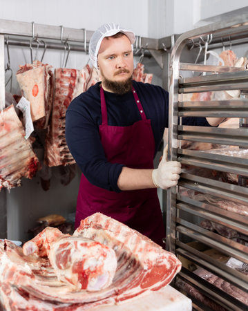 Portrait of male butcher while working in a butcher shop - moving trays with chopped carcasses