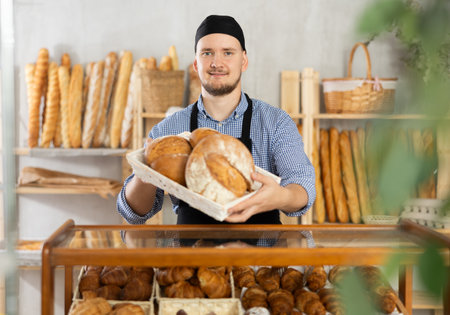 Male baker demonstrating delicious loaves of bread in bakeryの写真素材