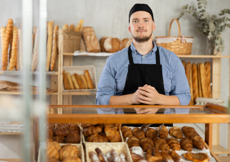 Portrait of a positive baker in an apron against the background of display case with fresh croissants aの写真素材