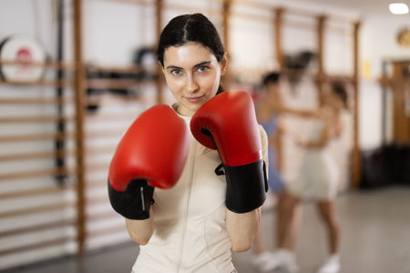 Girl coach in boxing gloves is standing in gym