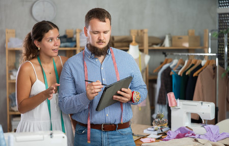 Young dressmakers sketching on tablet together in sewing workshopの写真素材