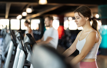 Girl performs exercises with stationary bicycle in gymの写真素材